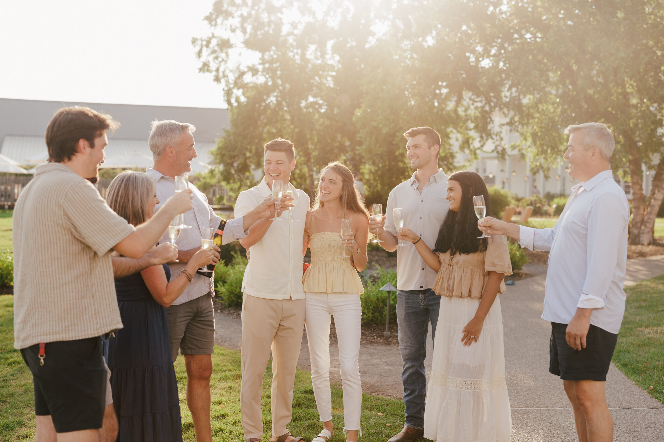 A smiling couple embracing during an outdoor engagement photoshoot at sunset, with soft golden hour light filtering through the trees.